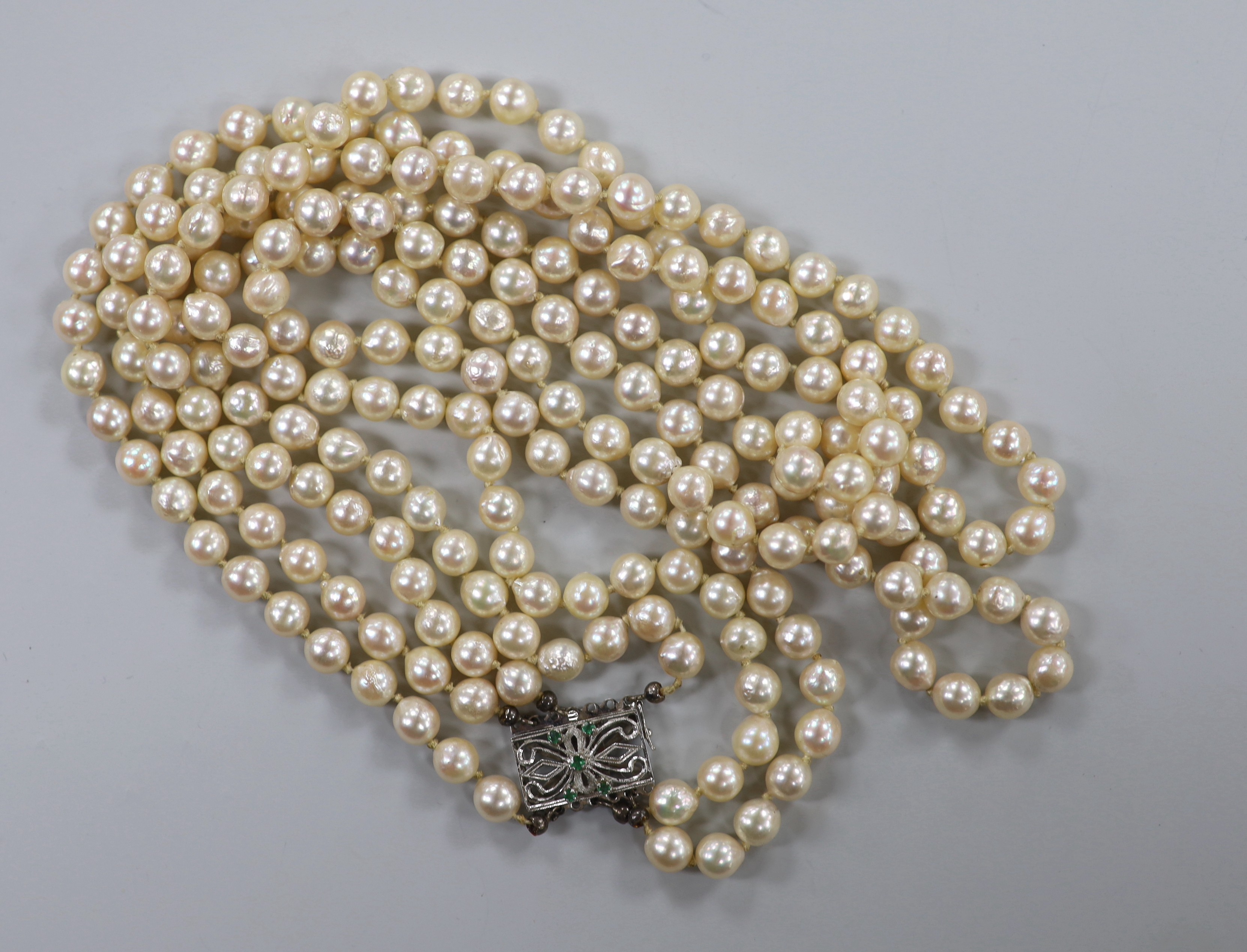 A mid to late 20th century triple strand cultured pearl necklace, with pierced 750 white metal and five stone emerald chip set clasp, approximately 56cm.